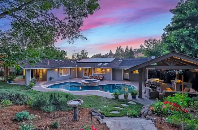 Backyard outdoor living space in Alamo, CA with pool, covered patio and lit landscaping at dusk