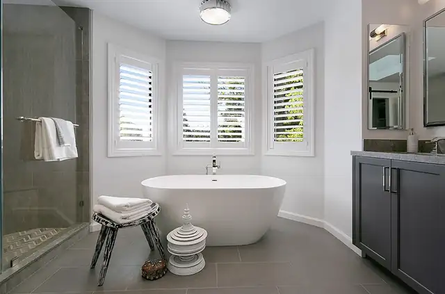 Primary bathroom in Danville, CA with freestanding soaking tub under shuttered bay windows and a charcoal vanity